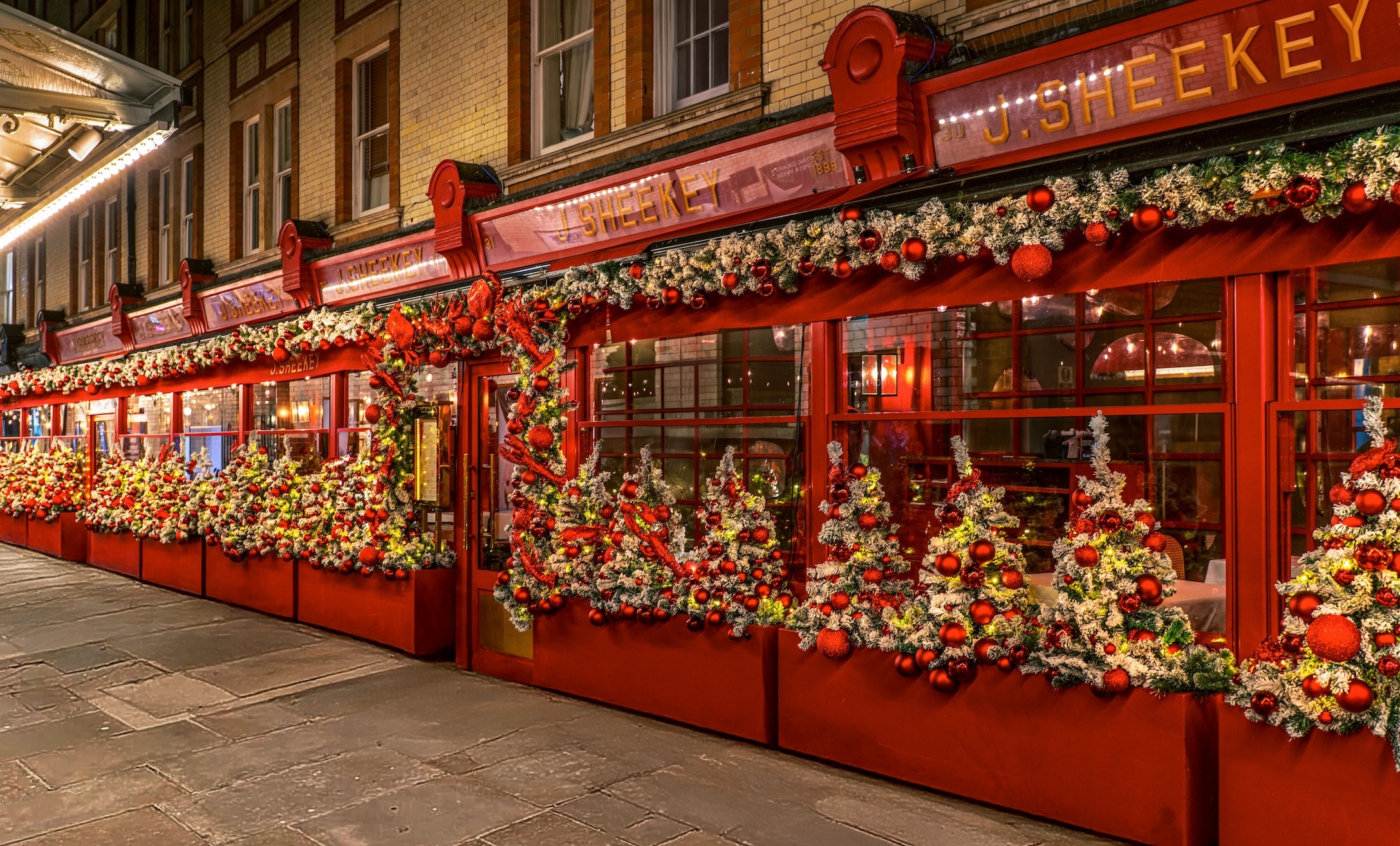 A restaurant exterior decorated for Christmas with red paint, festive garlands, baubles, and small artificial Christmas trees adorned with ornaments and lights—an ideal spot to include in your London weekend guide this December.