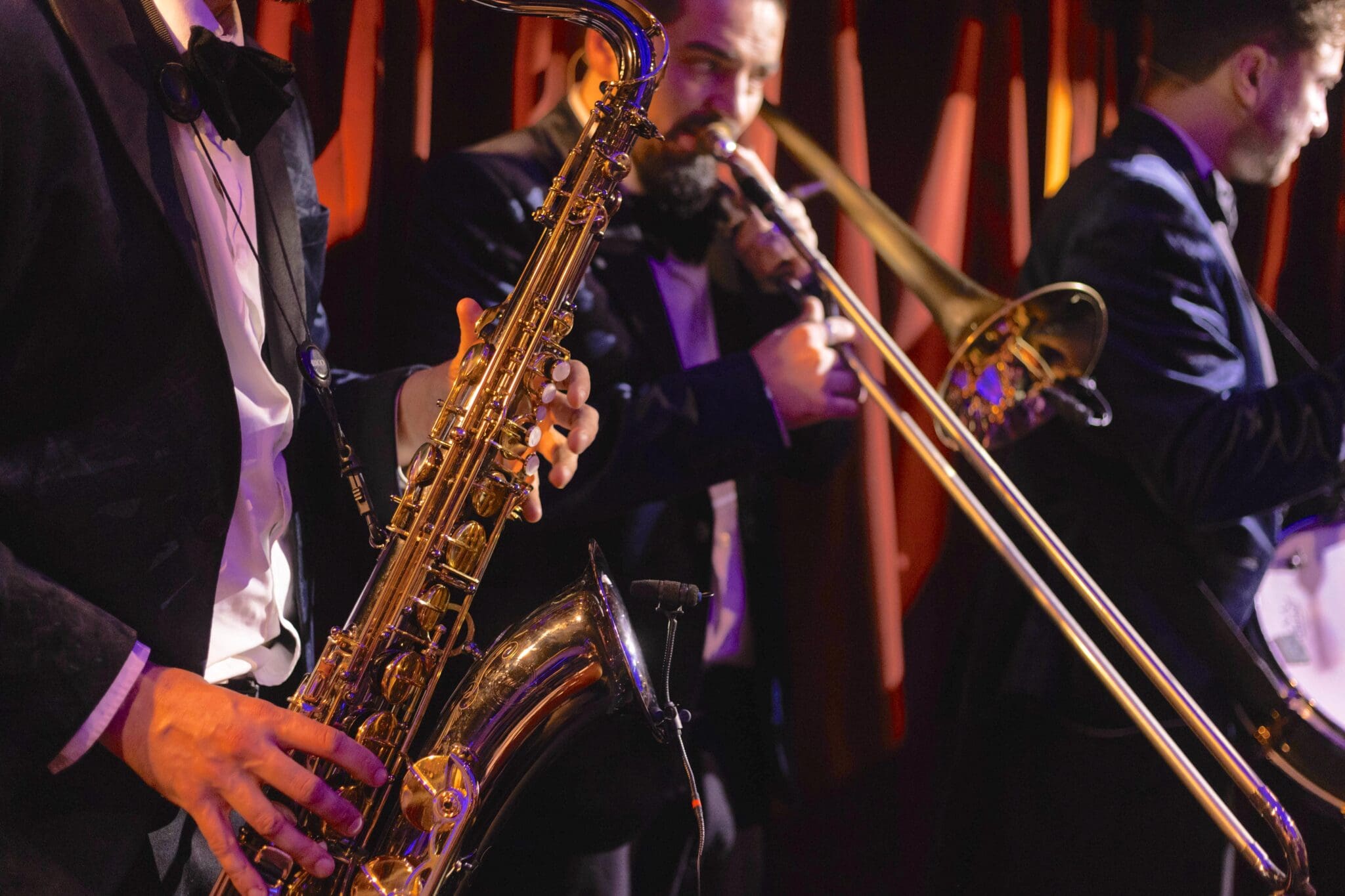 Three musicians in suits play brass instruments, including a saxophone and trombone, on a dimly lit stage with warm, orange lighting—an atmospheric highlight for any London weekend guide December edition.