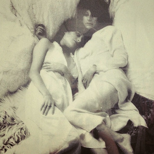 Two people in light clothing lie close together on a bed, their bodies and faces gently touching. The soft, slightly blurred image evokes a dreamy atmosphere, reminiscent of an editorial scene from Life In Fashion.