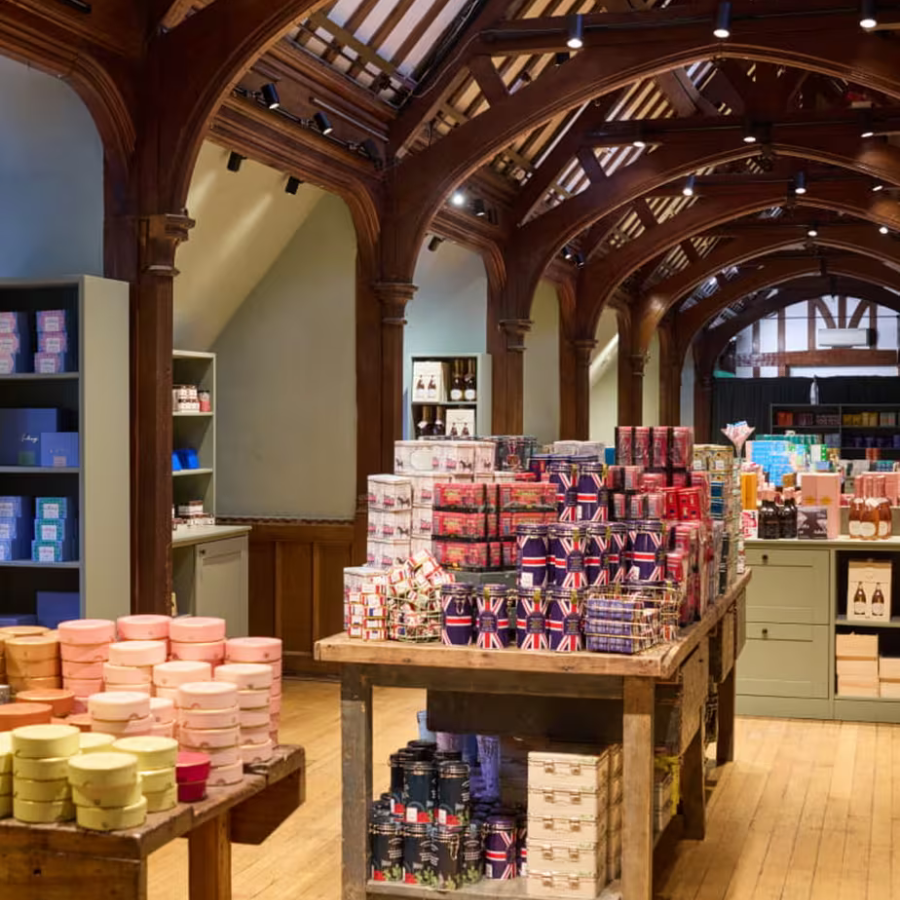 A shop interior with wooden beams and high ceilings, displaying neatly stacked gift items—including tins with Union Jack designs—on rustic tables and shelves; perfect for browsing unique finds during rainy day London explorations.