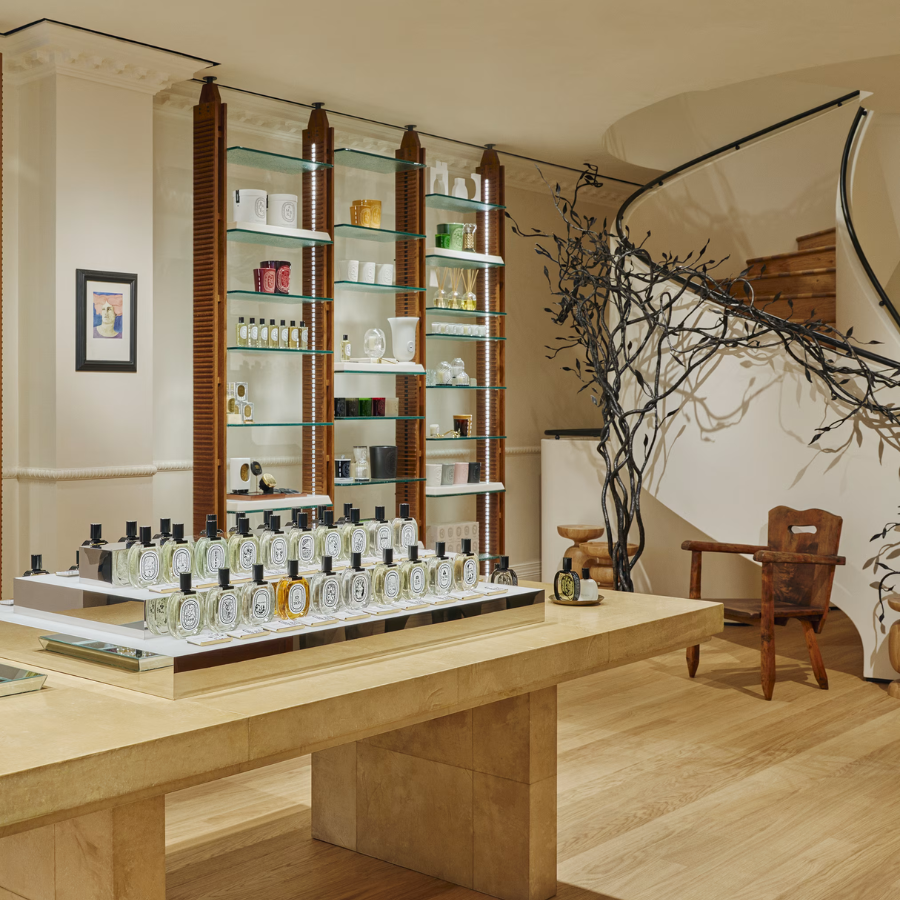 A luxury boutique interior with wooden floors, a display table of assorted perfumes, a glass shelving unit with home fragrance items, and a decorative spiral staircase—perfect inspiration for your next weekend guide.