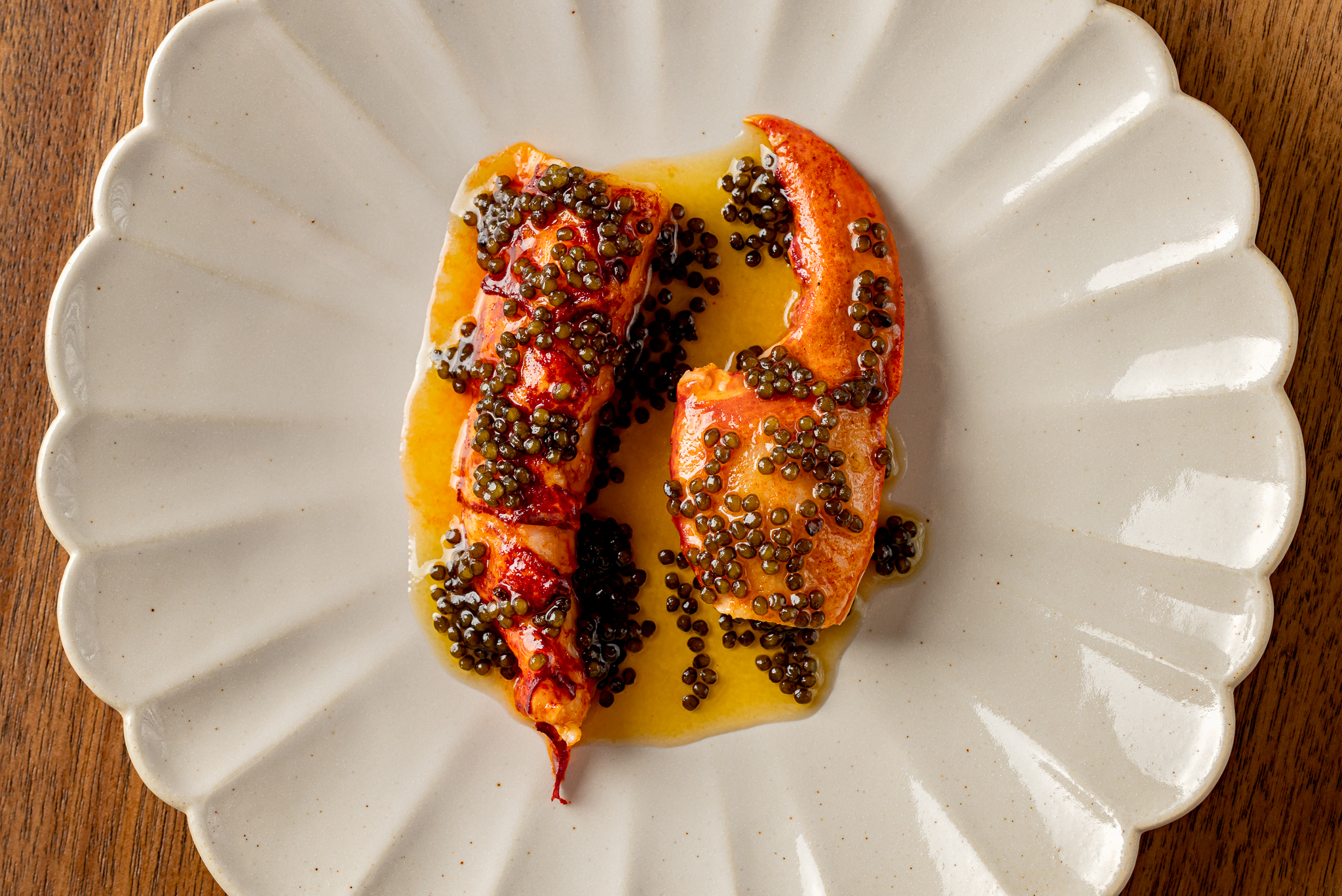 Two lobster claws covered in caviar and golden sauce, served on a scalloped white plate atop a wooden table—an elegant highlight of our affordable tasting menu.