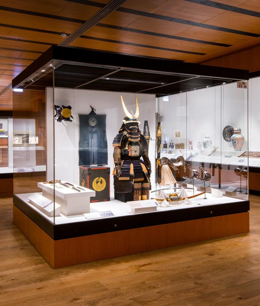 A museum display case featuring traditional Japanese samurai armour with a horned helmet, weapons, and artefacts—an inspiring highlight in a modern, well-lit gallery with wooden floors. Add this to your weekend guide for an unforgettable cultural experience.