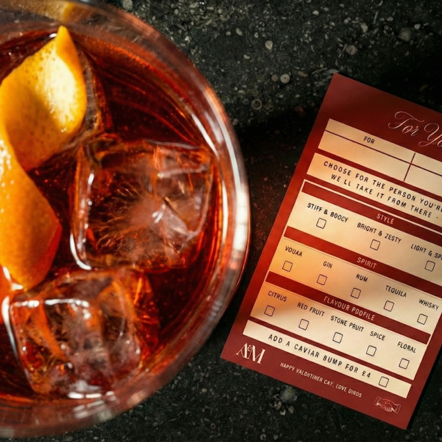 A glass of cocktail with ice and orange peel sits next to a red menu card offering options to customise a drink, making it the perfect weekend guide for crafting your ideal style, spirit, and flavour profile.