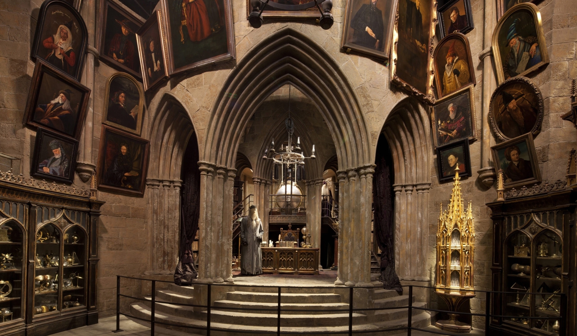 A large, ornate stone room with arched doorways, grand steps, and walls covered in framed portraits evokes the charm of a Harry Potter restaurant. Glass display cases hold artefacts, and a golden structure hints at a magical, historical setting.