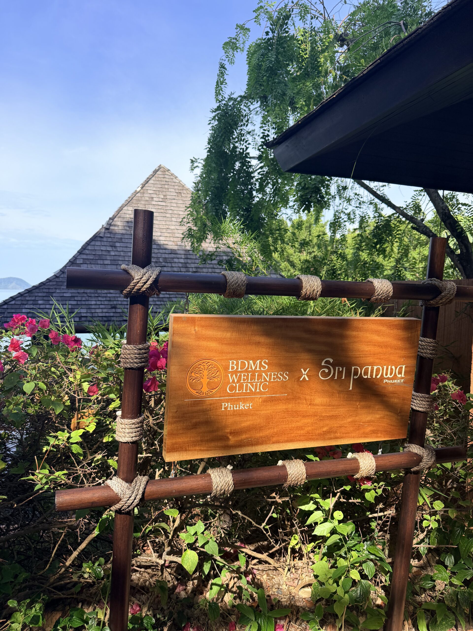 Wooden wellness retreat sign surrounded by tropical greenery and flowers at a luxury Phuket spa and wellness destination.