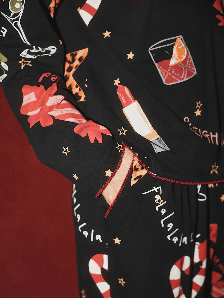 Close-up of Rockett St George black pyjamas with a festive print including lipstick, candy canes, cocktail glasses, gift bows, and Fa la la la la text.
